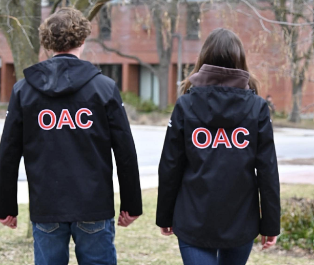 Two students wearing black jackets with OAC in red lettering on the back