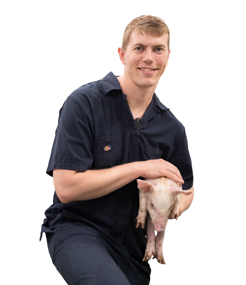 Conor Voth smiling at the camera while holding a piglet
