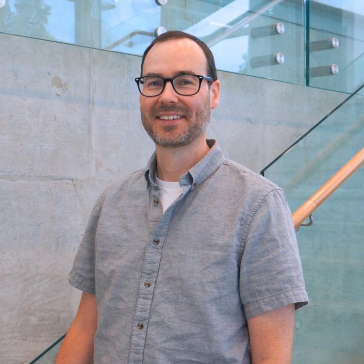 man standing in a glass and wood stairwell smiling