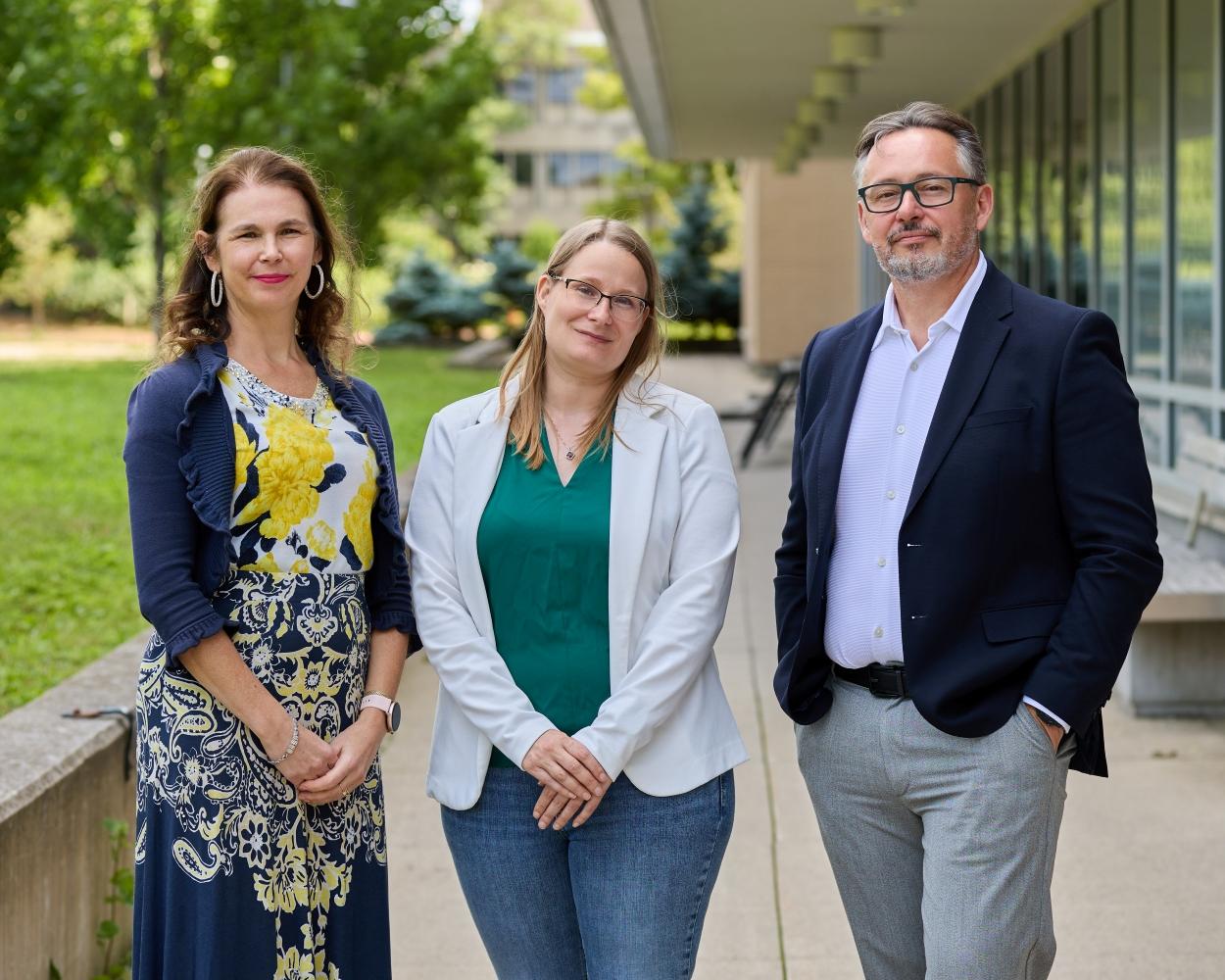 Three people posing for the camera outside with a building behind them.