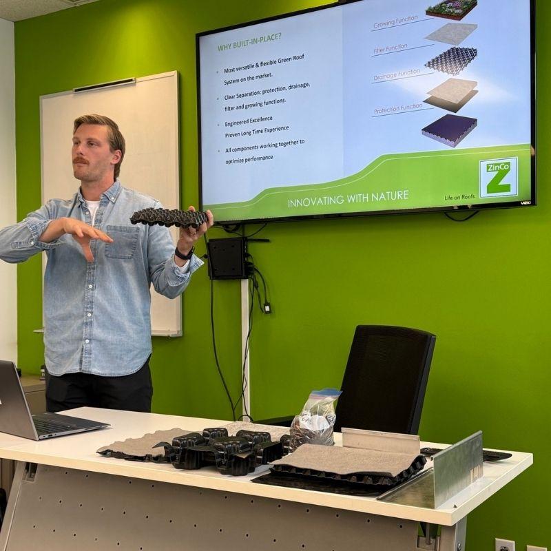 Guelph Grad Jordan Hofstra presenting his green roof system standing in front of a room holding a sample