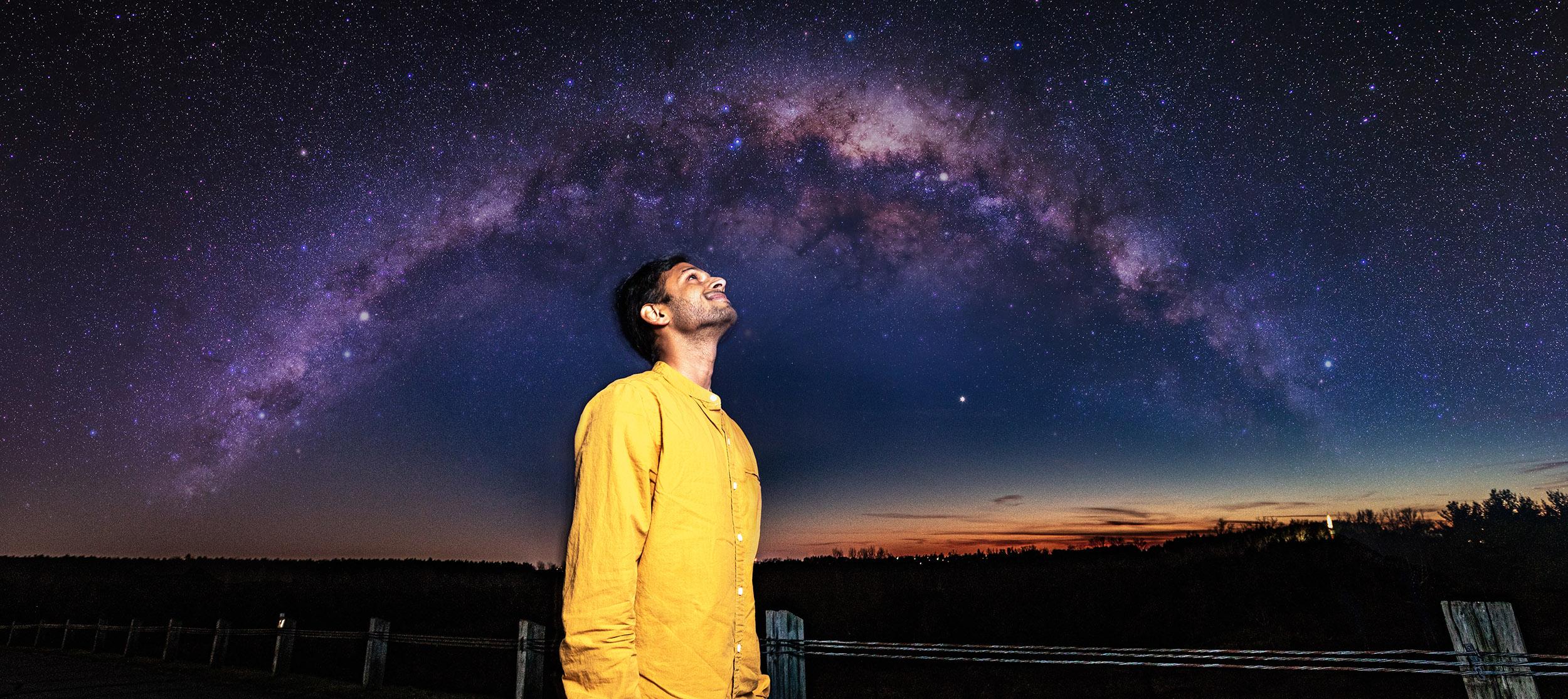 Aman stands under the night sky looking up.