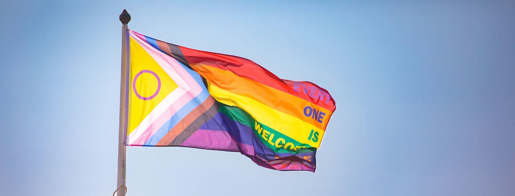 Pride flag flaps in the wind in front of a clear sky.