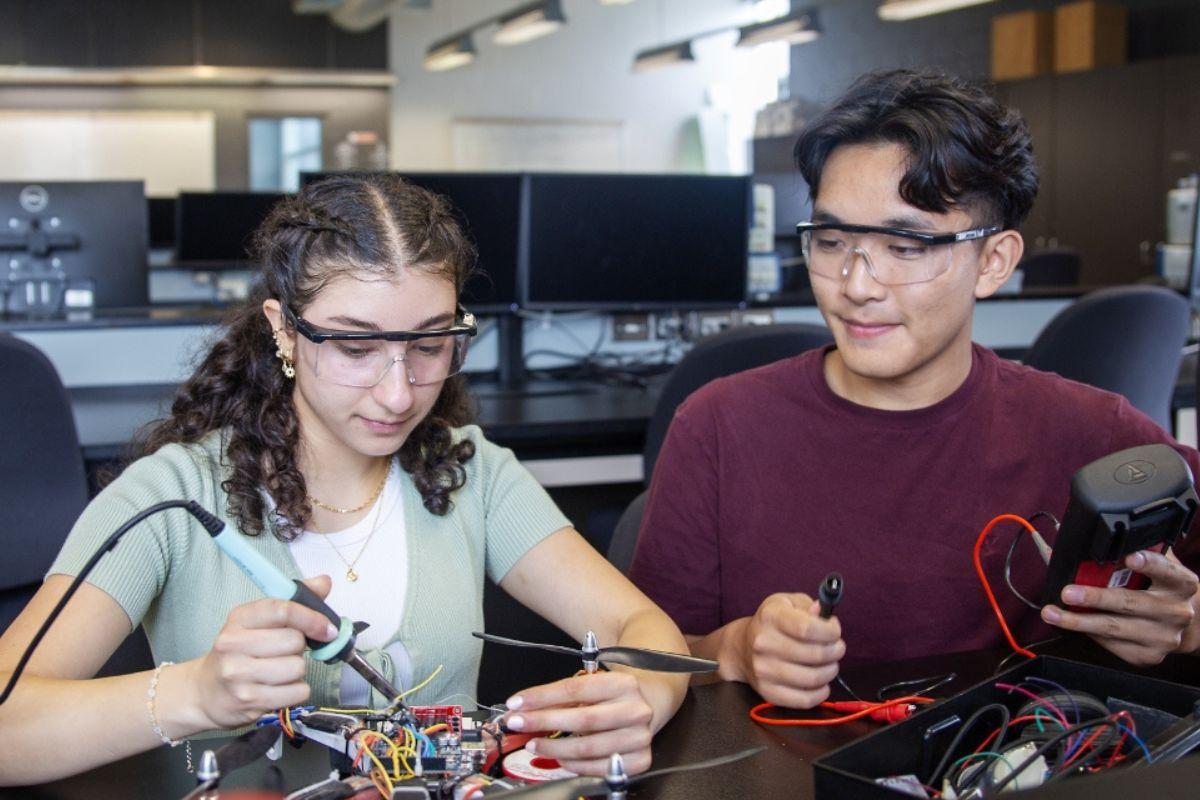 Two engineering students working together to solder a motherboard.