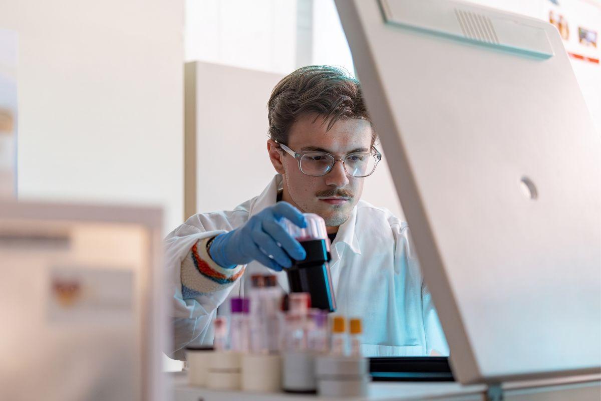 Student wearing safety glasses and a lab coat reviews samples in a lab
