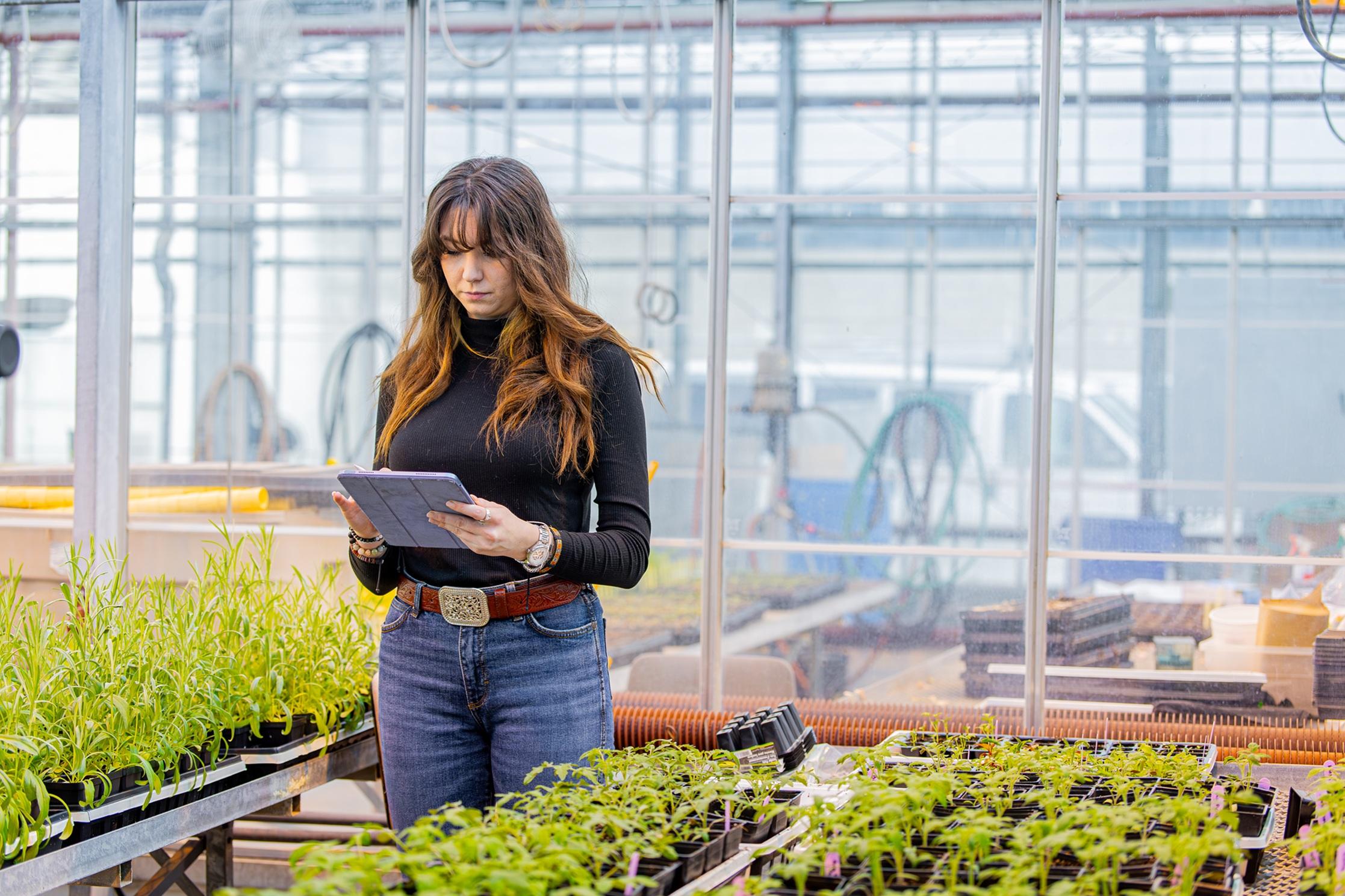 student in a greenhouse holding a tablet