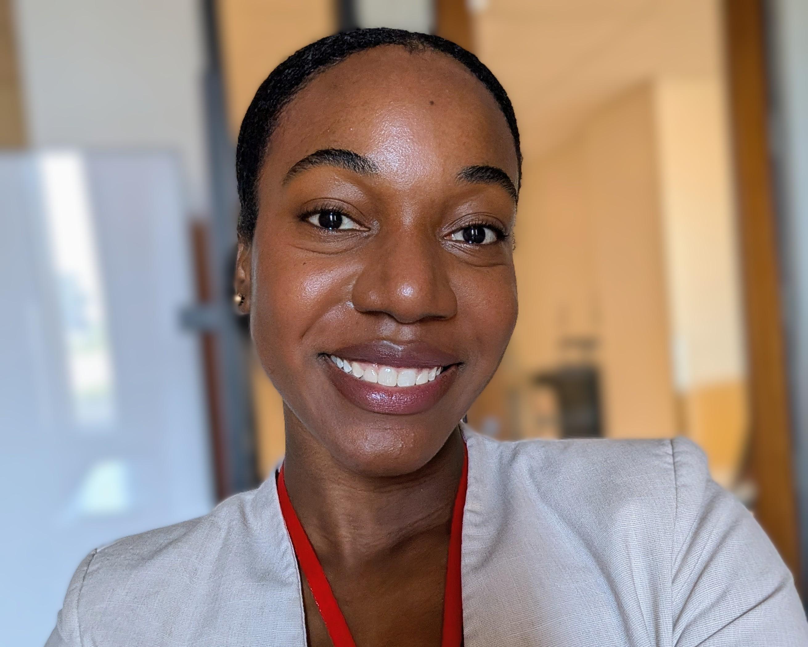 A headshot of a smiling woman with hair pulled back wearing a light colored blazer.