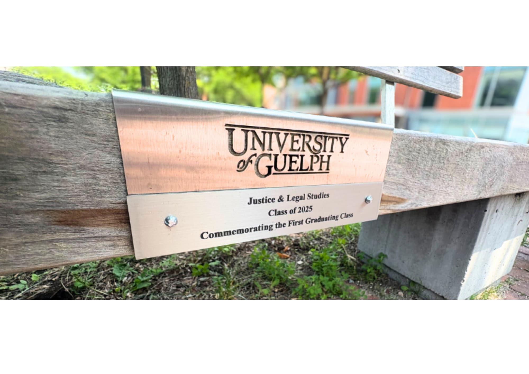 Close-up of a plaque on a wooden bench reading “University of Guelph, Justice & Legal Studies, Class of 2025, Commemorating the First Graduating Class.”