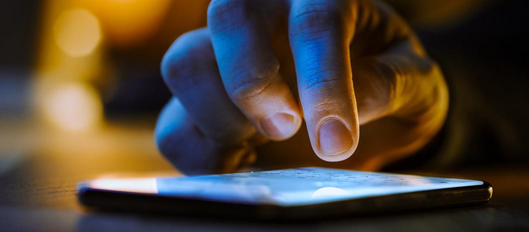 A person taps on a cell phone that is lying on a table (iStock credit_gorodenkoff)