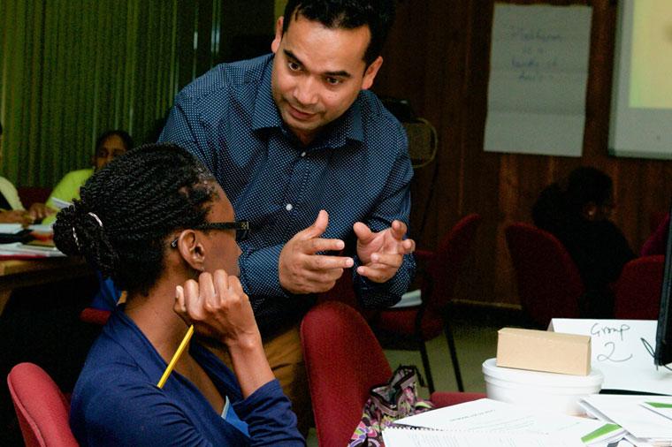 Professor leans down to speak with student working at a table