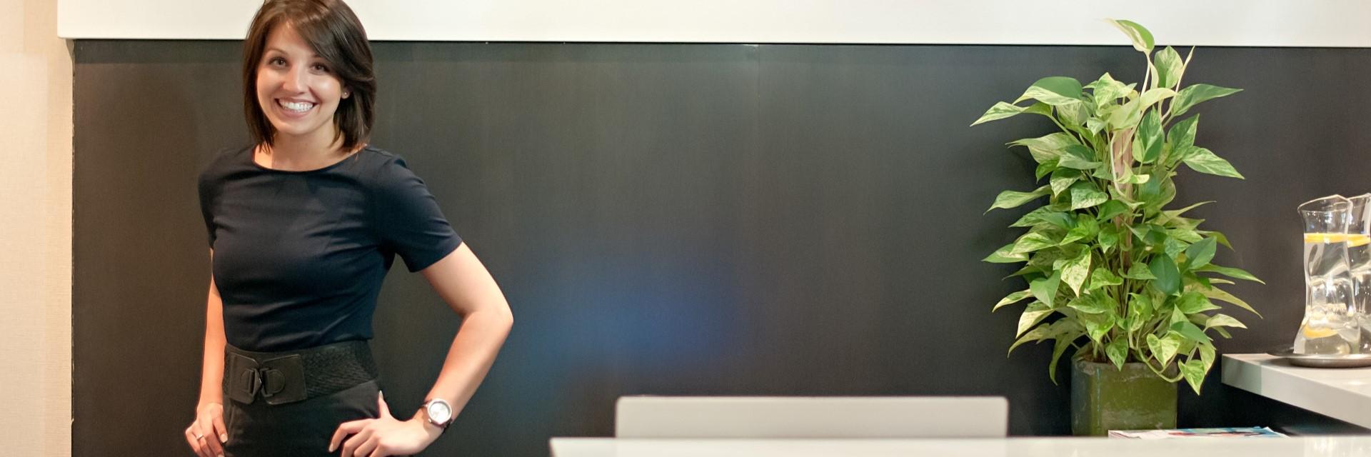 a person smiling, standing at a reception desk
