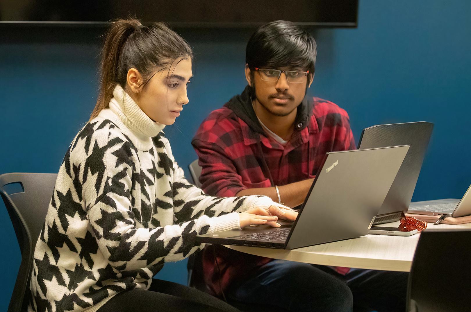 Two MCTI students in class working together on laptops.