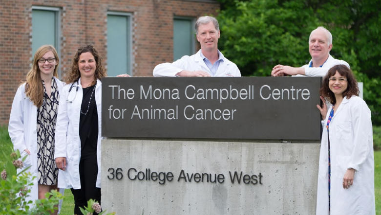 Five people wearing white lab coats standing around a sign outside of an animal cancer centre