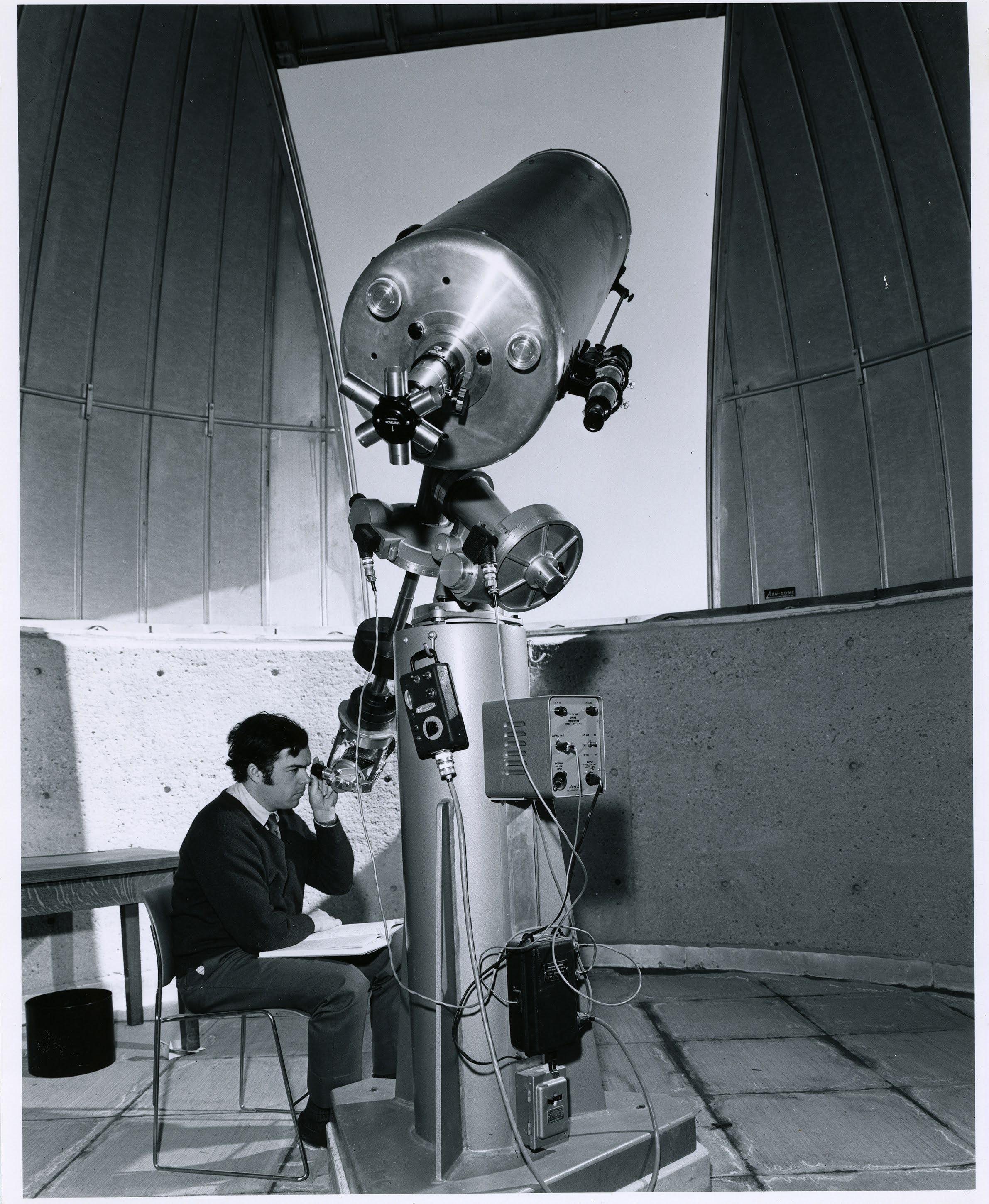 black and white, man seated at a large telescope with the observatory dome open