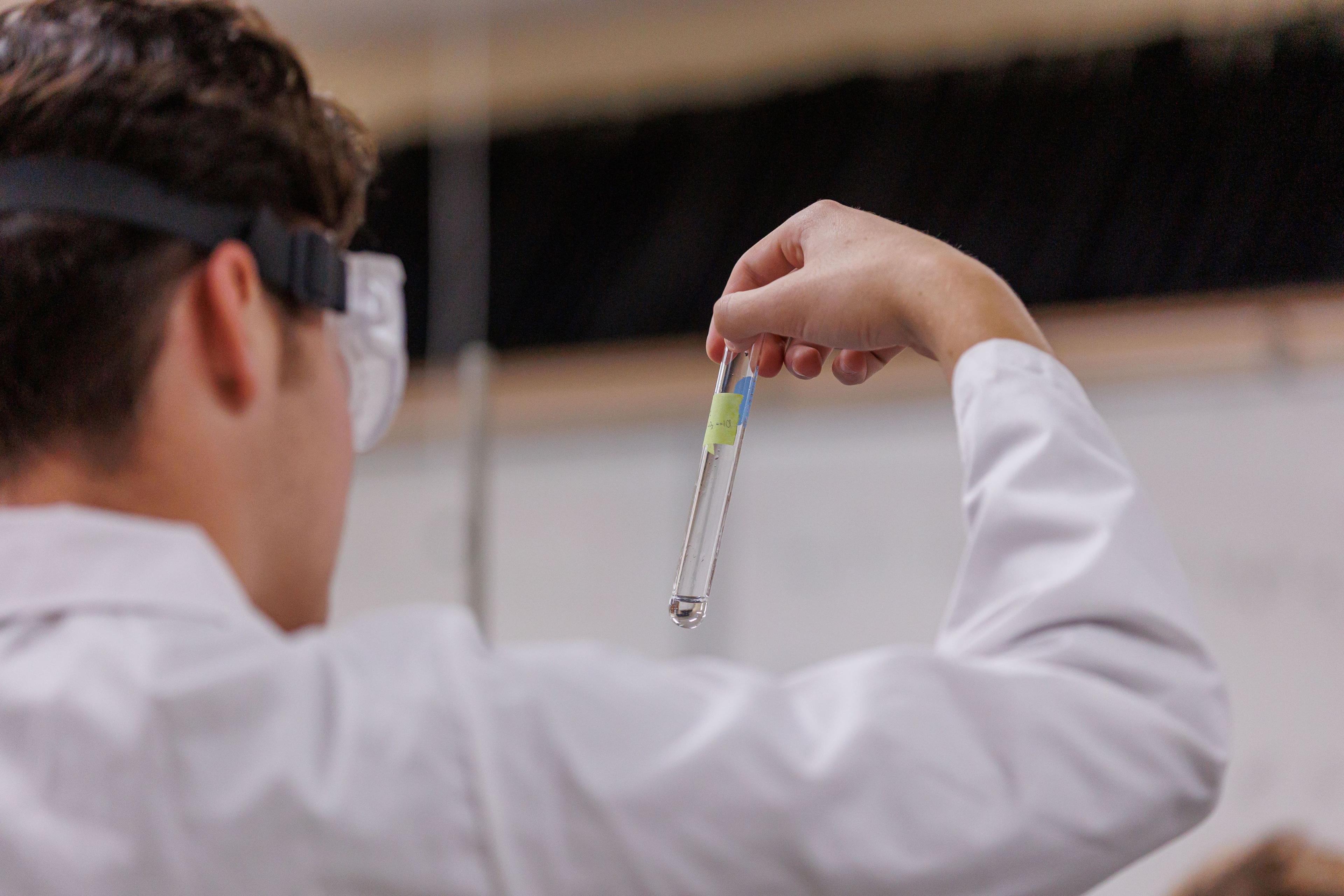 Student in lab gear analyzing a test tube.