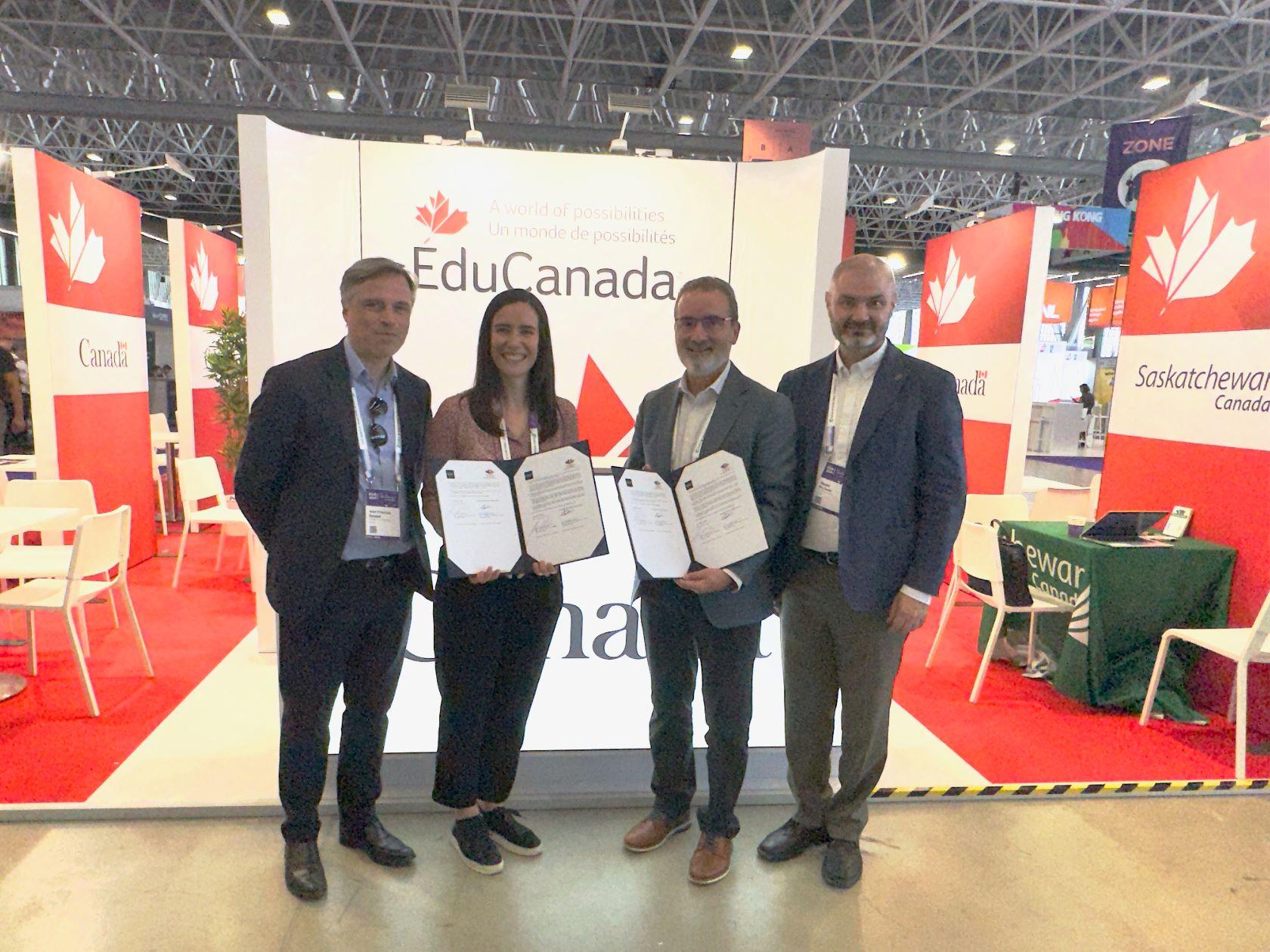 Four people stand in front of an Edu Canada banner, holding signed agreements in folders