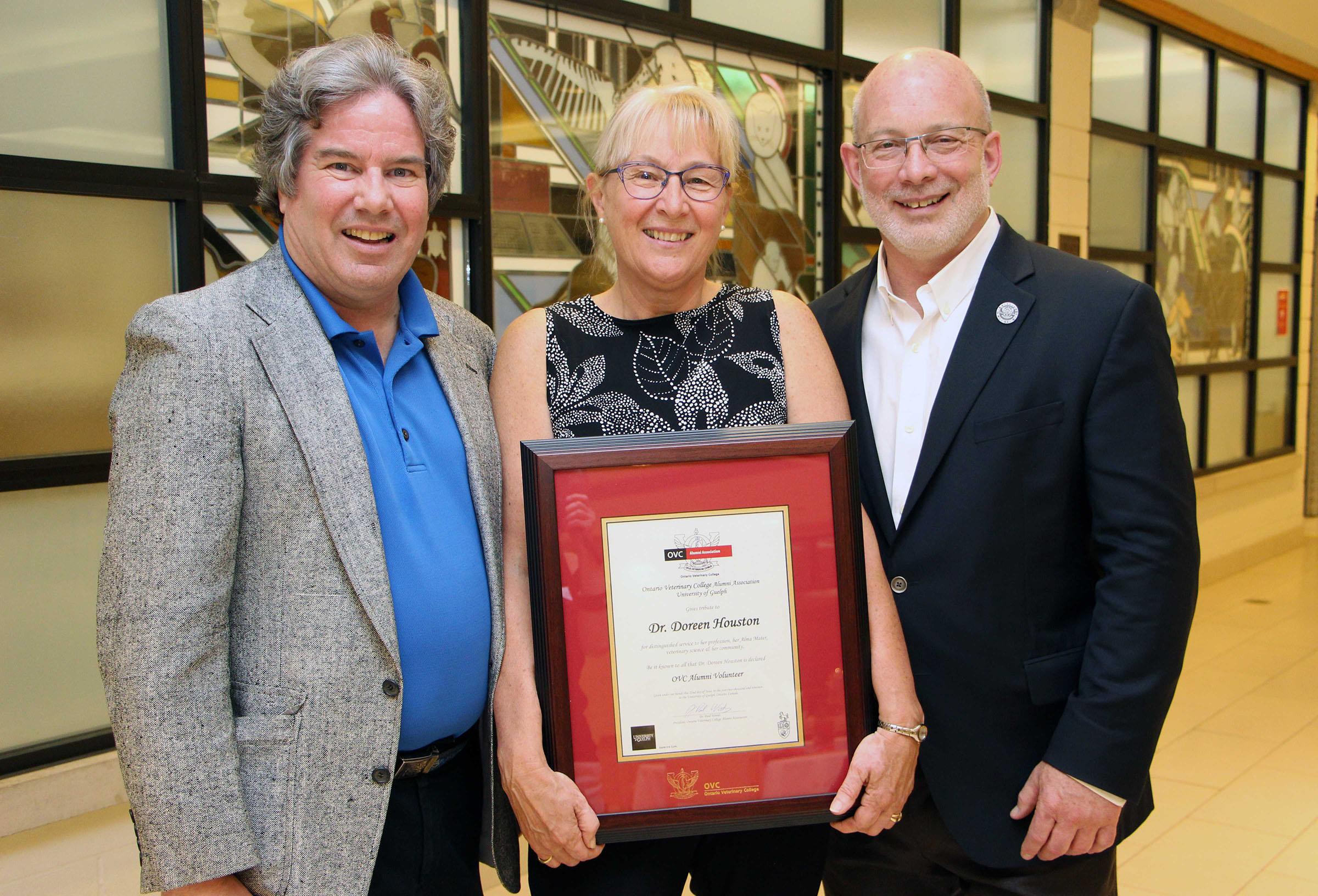 New grad standing and smiling holding their framed OVC degree next to two faculty