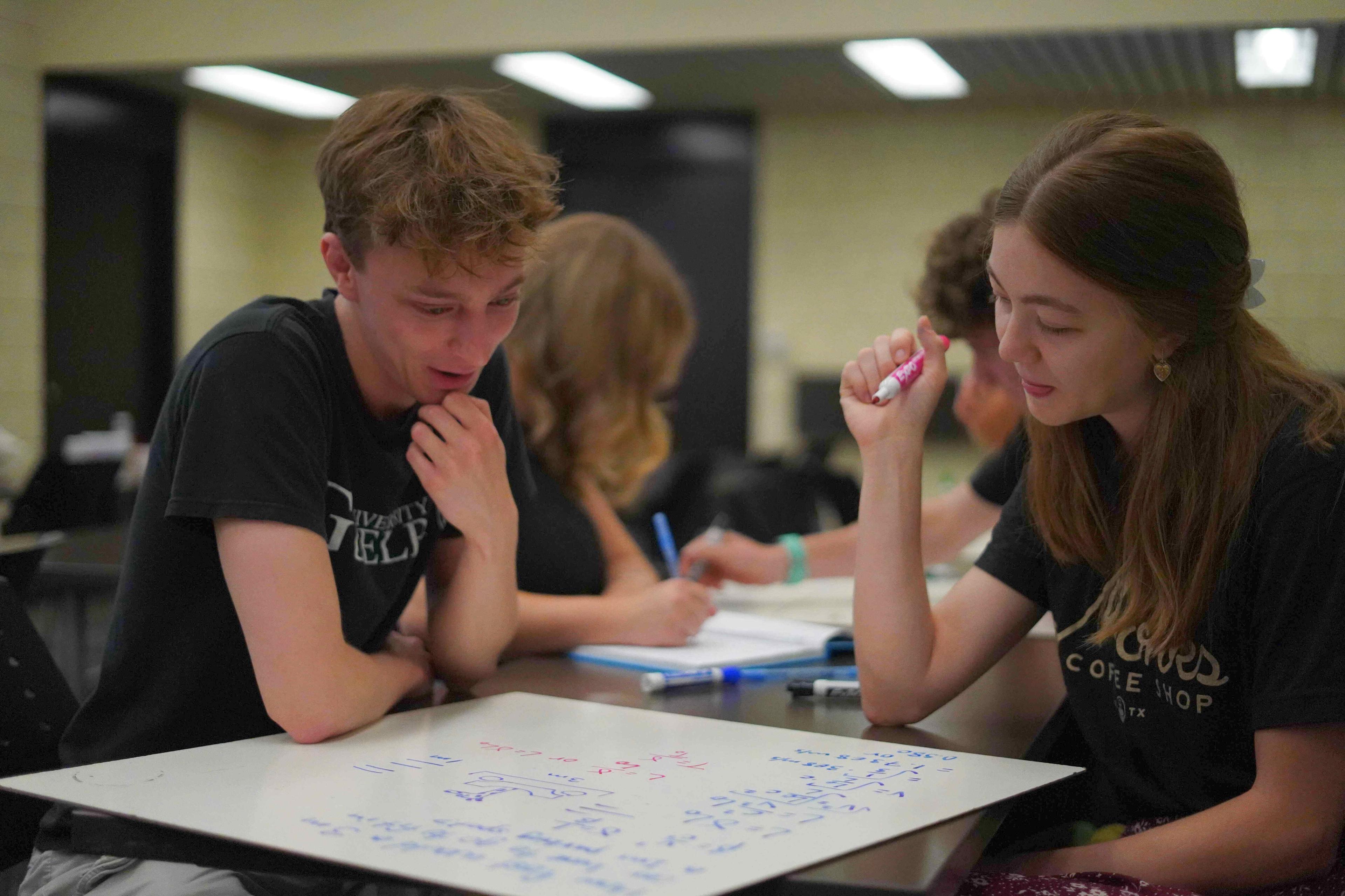 Two students sitting together writing on a white board.