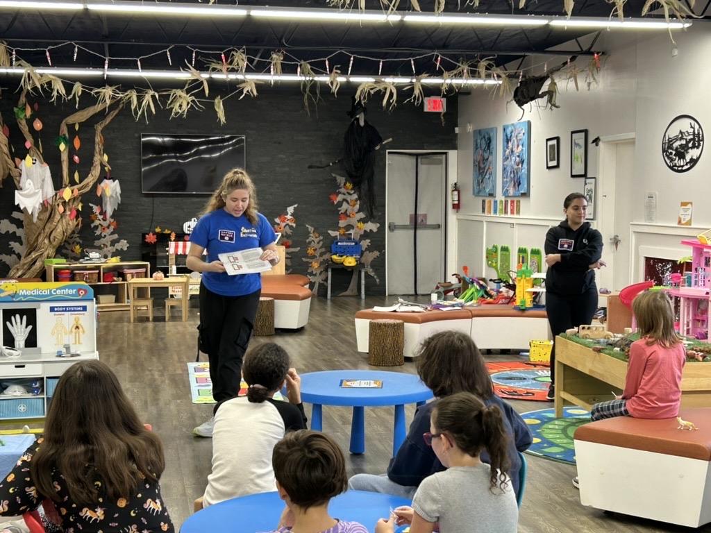 Image of two student instructors from the University of Guelph's Creative Encounters showing participants a demonstration at the Anishnabeg Outreach Centre.