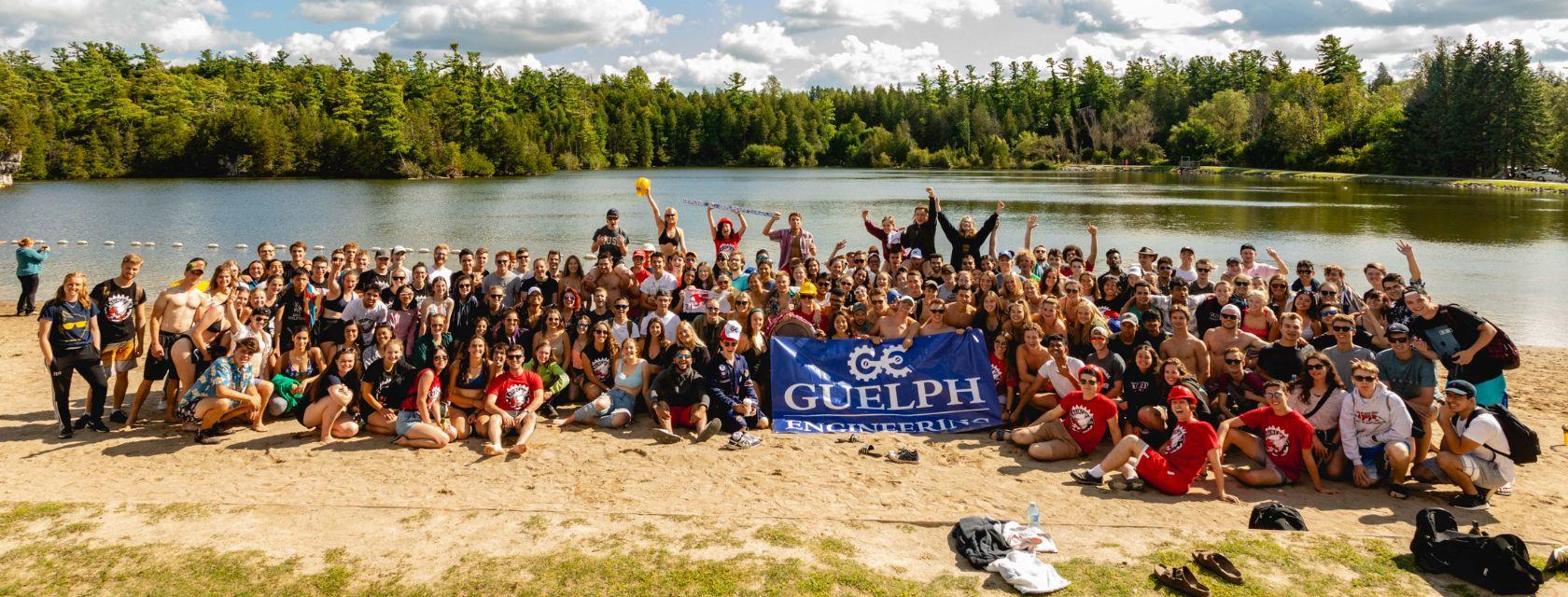 Large group of Guelph Engineering students pose on the beach at Guelph lake