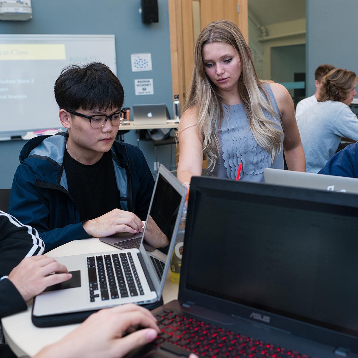 A man and a woman working in a group with other students using laptops