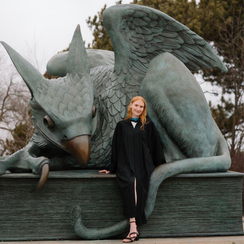 Applied Human Nutrition Grad Megan Rohde poses in front of a large gryphon statue while wearing her convocation gown..