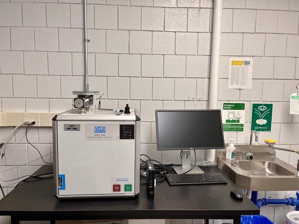 An elemental analyzer sits on a black desk next to a computer.