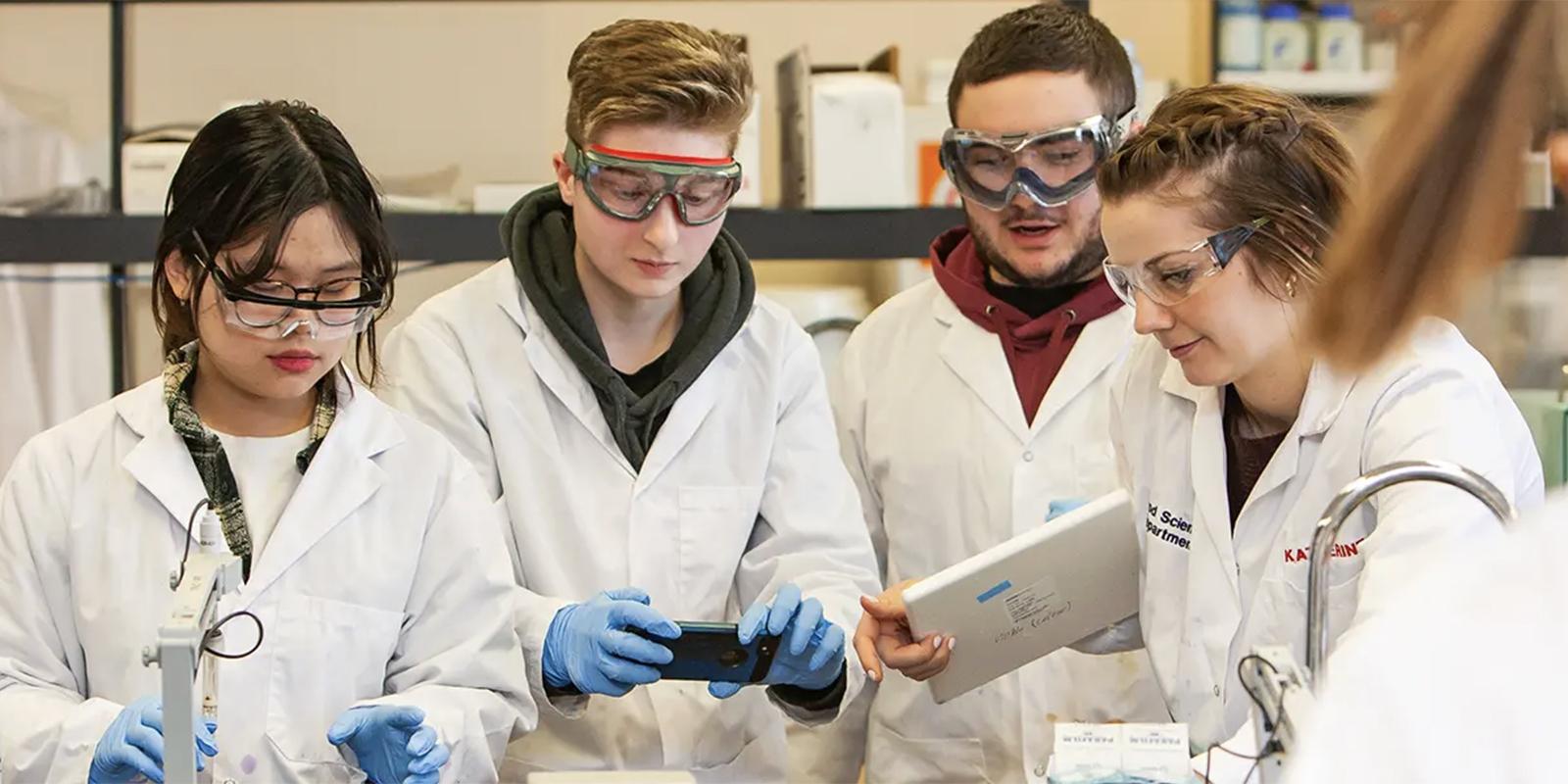 Four high school students in lab coats in a lab working on a project