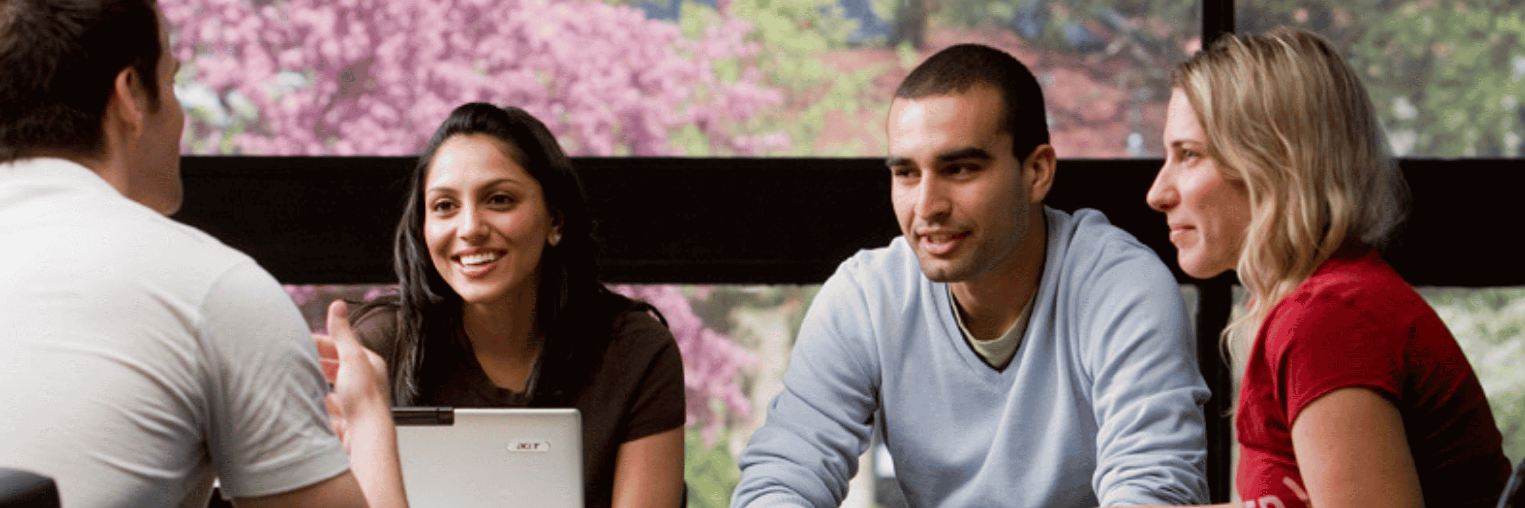 Group of four students sitting inside, with a window and trees in the background