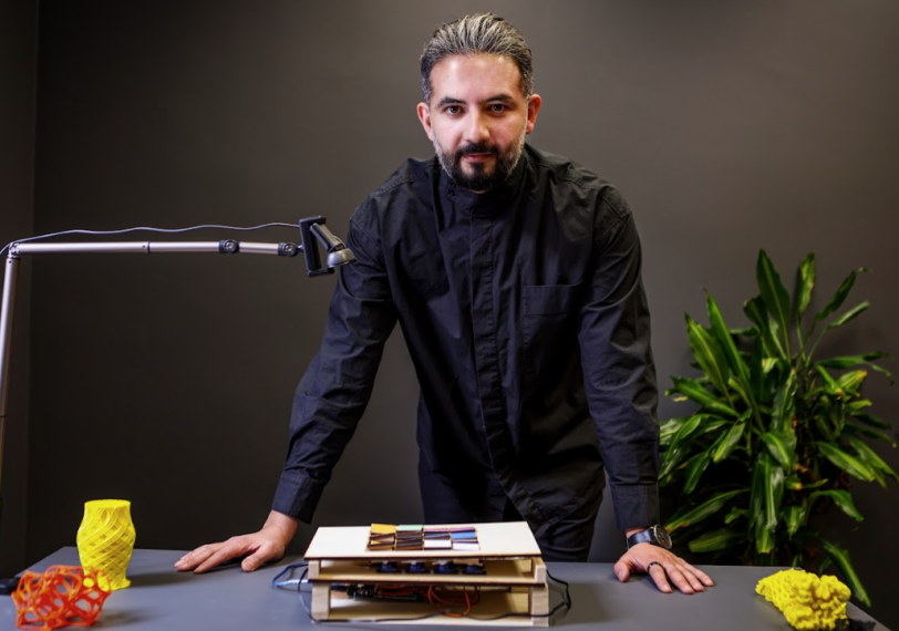 Professor Afshin Ashari in a black dress shirt with his hands on a desk that has a variety of 3D models