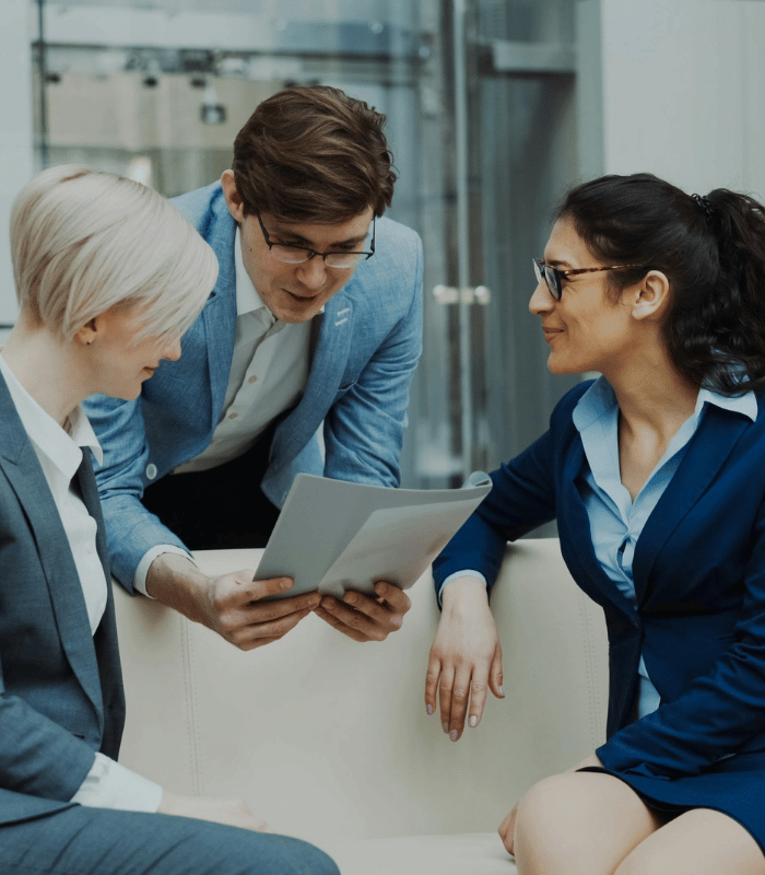Three people in business attire chatting and looking at a file