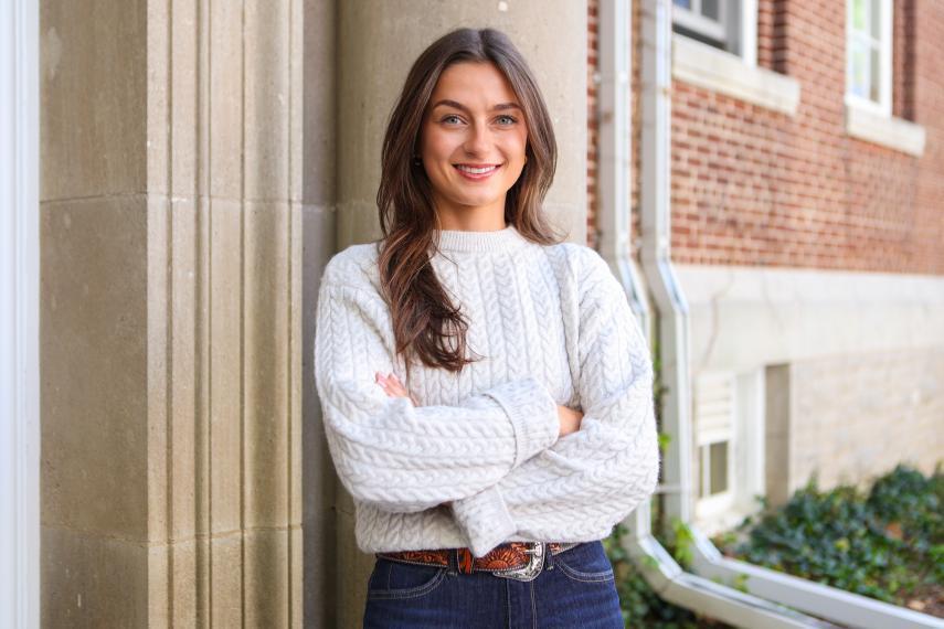 Julianna Tindall standing outside a building wearing a white sweater with her arms crossed