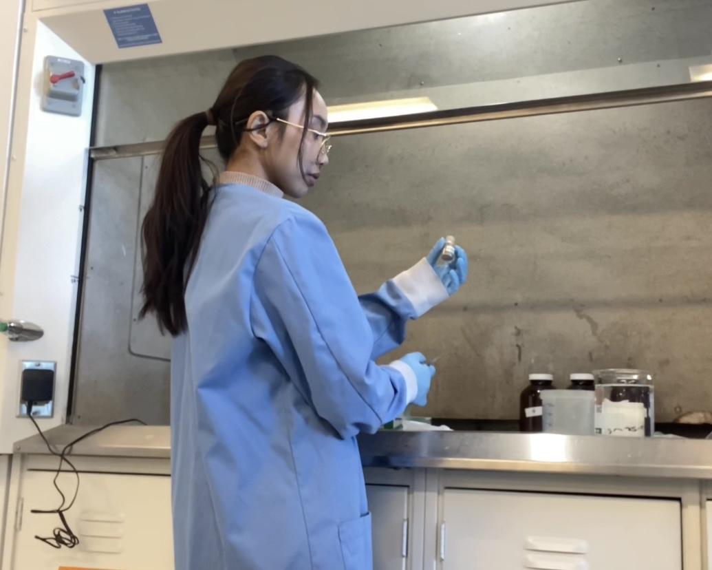 Student in a lab coat standing in lab holding a vial