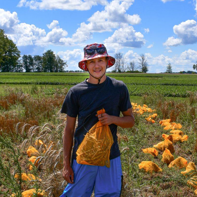 Riley McConachie standing in the wheat field on a sunny day holding an orange bag