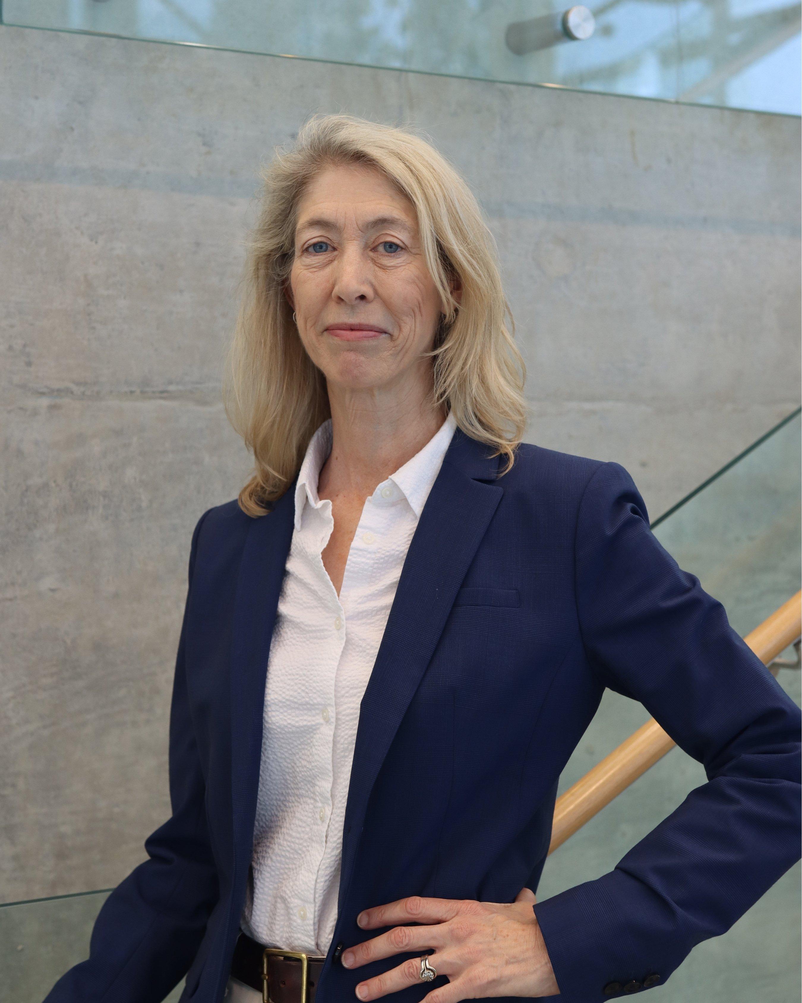 Dr. Carolyn Kerr- A tall white woman with blonde hair posing for a headshot with one hand on her hip on the pathobiology stairs