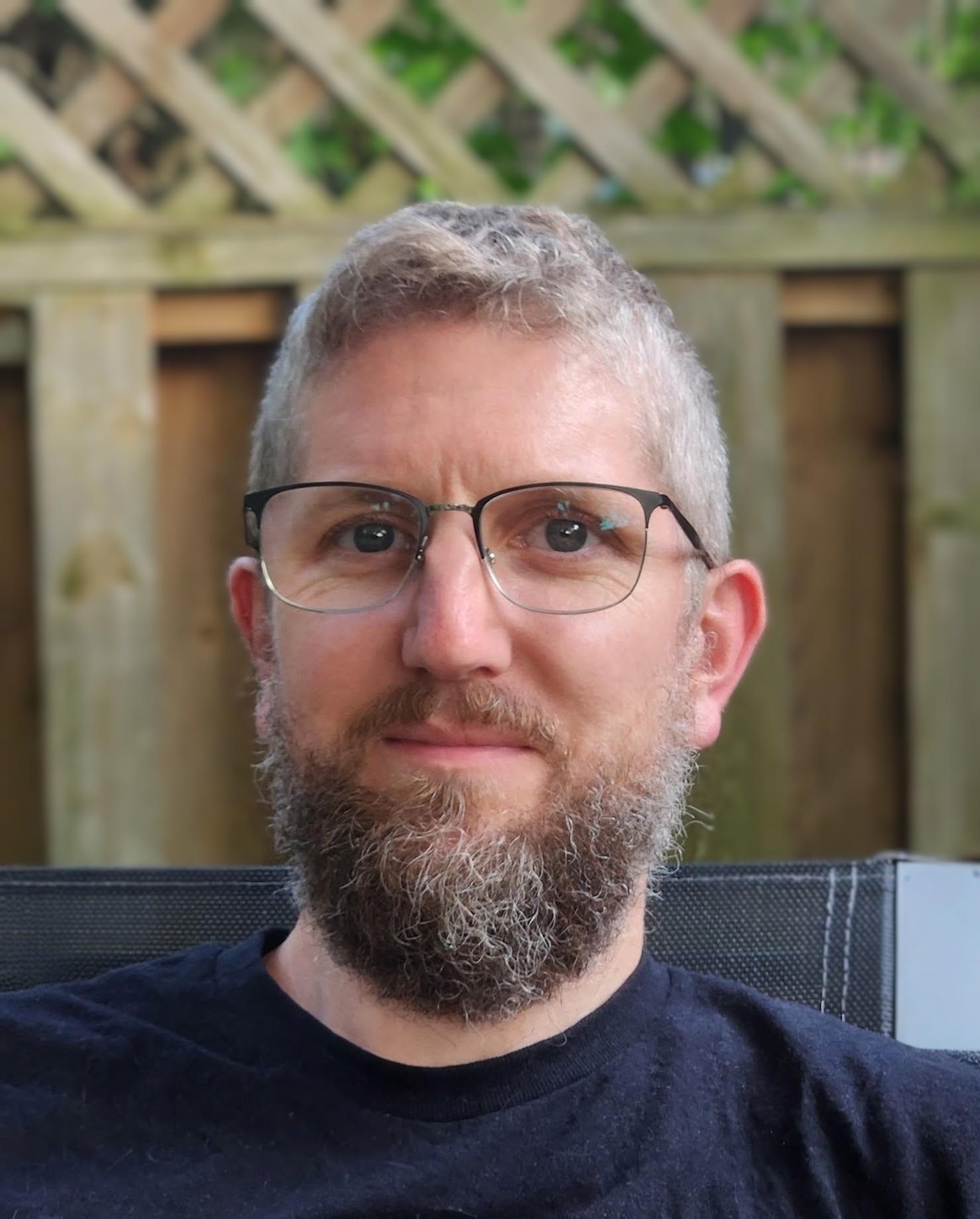 A photograph of Kevin Courtney, a man with a beard and glasses