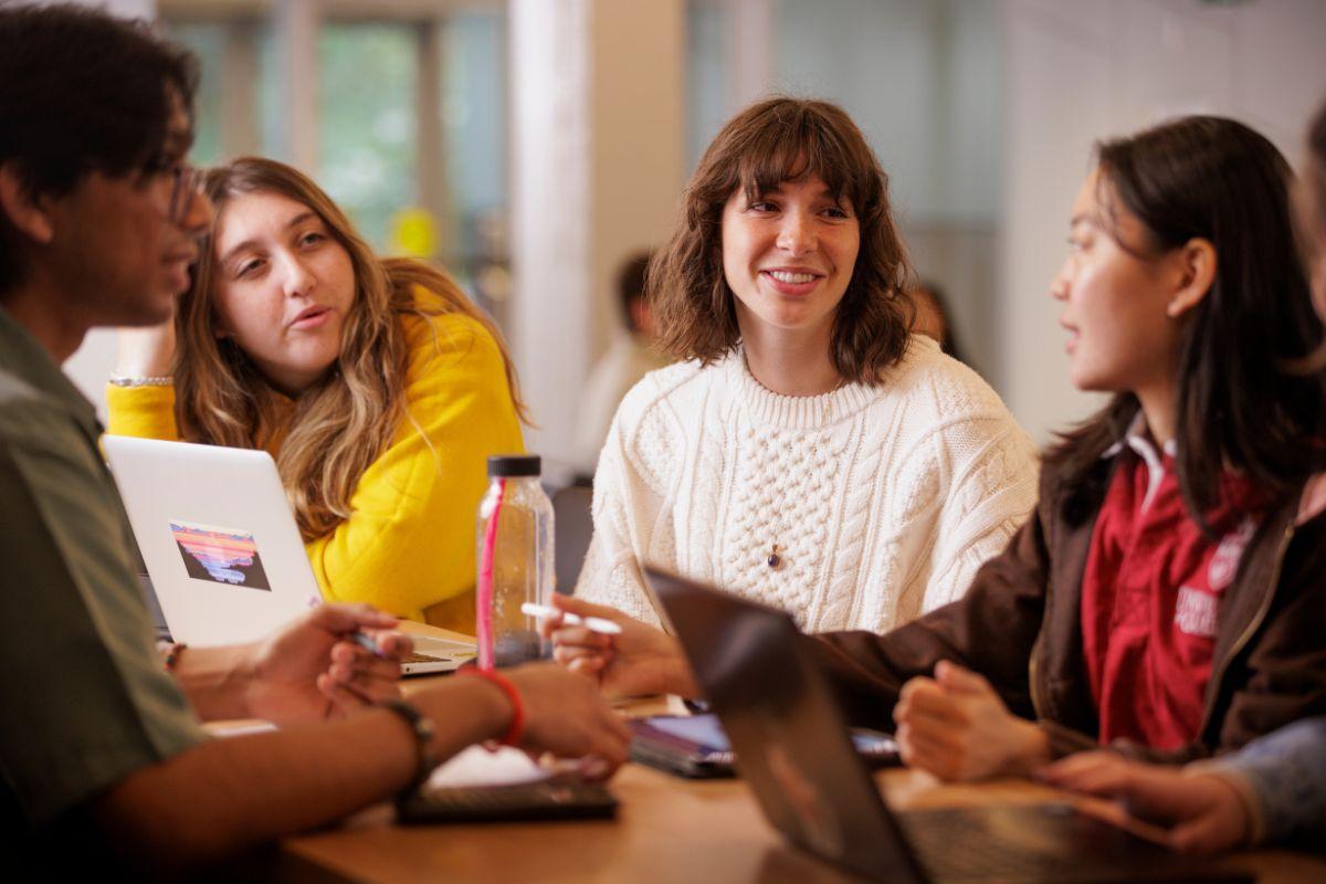 A group of students gathered at a table each with laptops in deep conversation