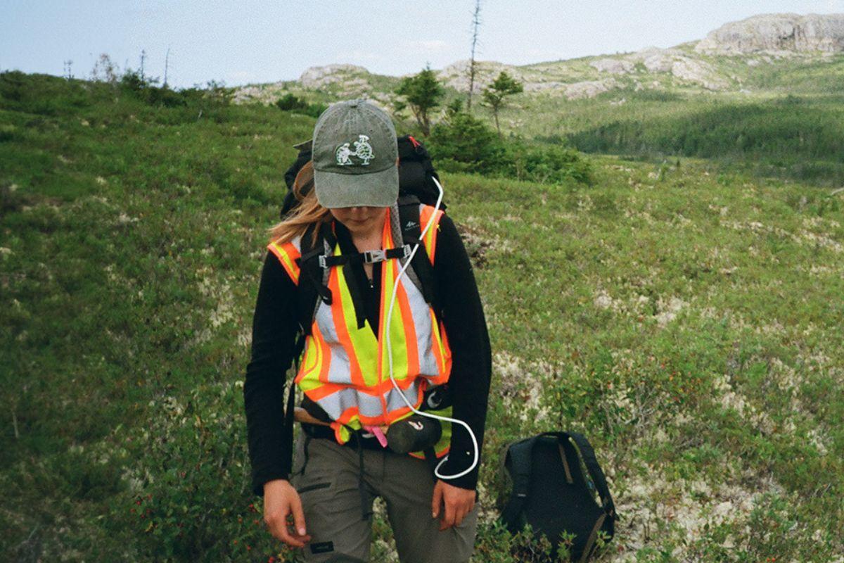 Girl wearing a safety vest hikes across a green mountain side