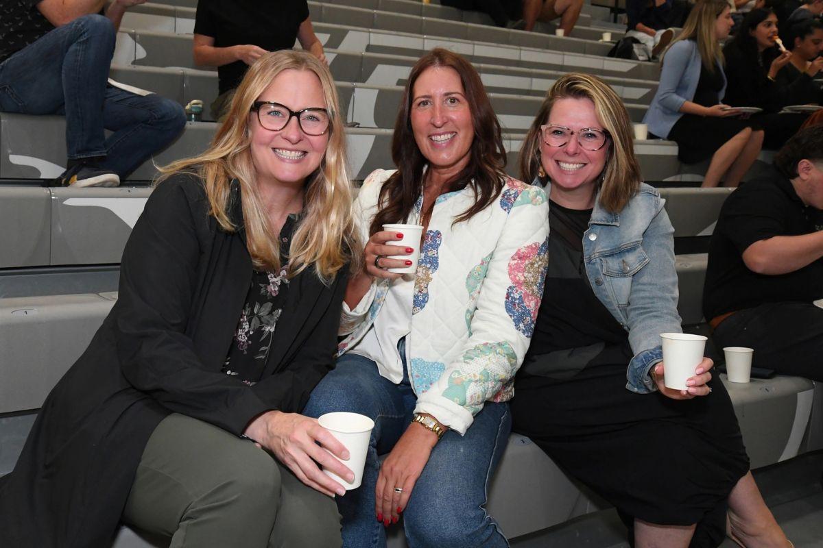 A group of 3 women smiling and sitting closely together while at a staff event
