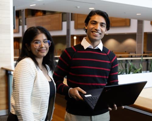 Two students standing with a laptop