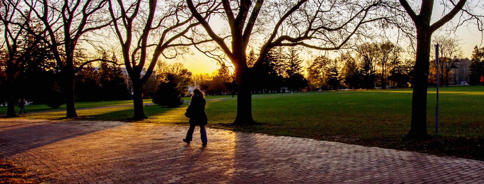 Student walking across a quiet campus at sunset.