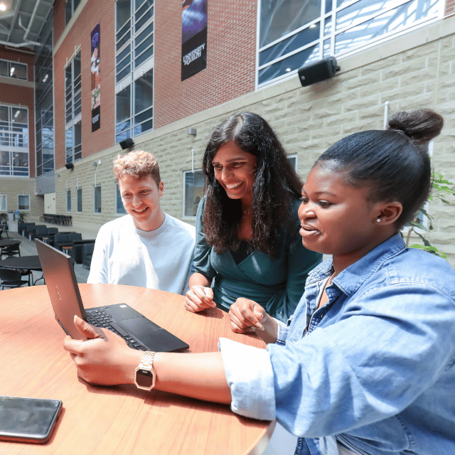 Three students are looking at a laptop.
