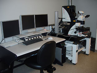 Image of a CLSM SP5 confocal microscope to the right of a desk with three white monitors on top
