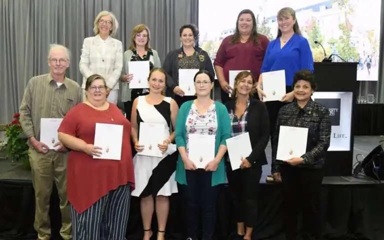 Ten staff members stand smiling with President Yates, all holding their awards for exemplary service.