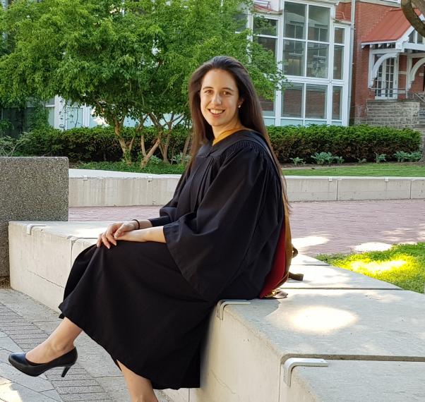 Photo of Anna Schwanke sitting on a stone bench wearing graduation robes.