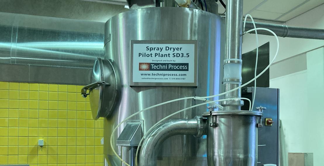 Close-up of a large metal cylinder, taller and wider than a person, labelled Pilot Plant SD3.5 with the brand name TechniProcess