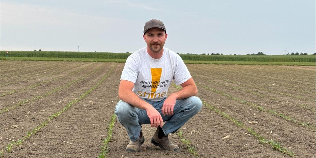 Technician Ted Vanhie wears a baseball hat and jeans and squats in a field with seedlings sprouting