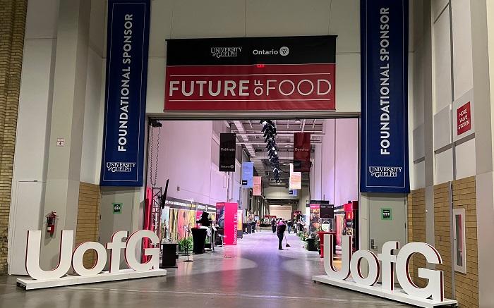 Looking into the U of G exhibit at the Royal Agricultural Winter Fair. Two "UofG" signs flank the entrance of a large hall with high ceilings. A banner with "The Future of Food" hangs above.