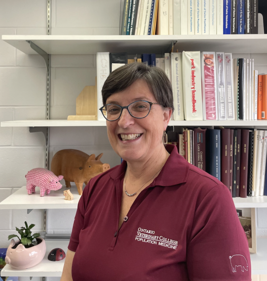 Dr. Anne Deckert stands in front of a bookshelf, smiling