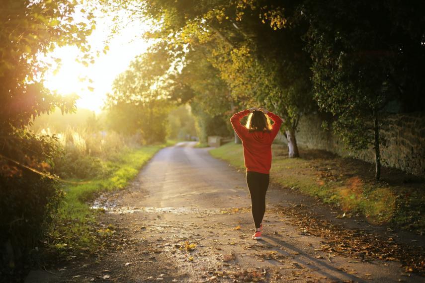 A woman walks away from the camera along a rural path with her hands on her head